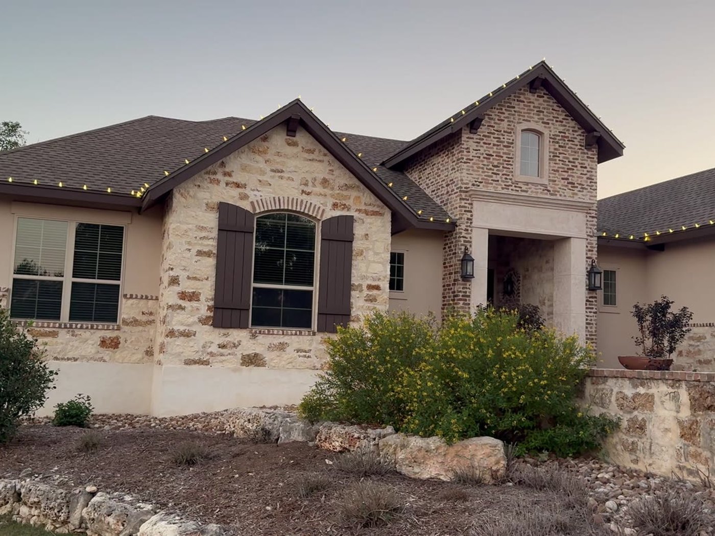 Stone home at dusk with C9 Christmas lights running the length of the eaves and gables